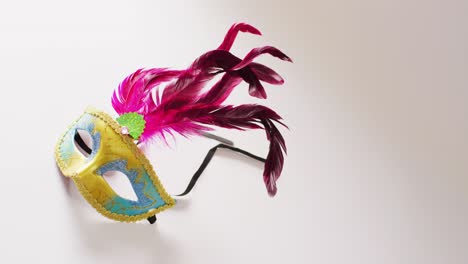 Video-of-yellow-and-blue-masquerade-mask-with-pink-feathers-on-white-background-with-copy-space