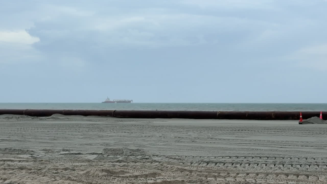 Panning view, pipe pumping sand from ocean, beach replenishment