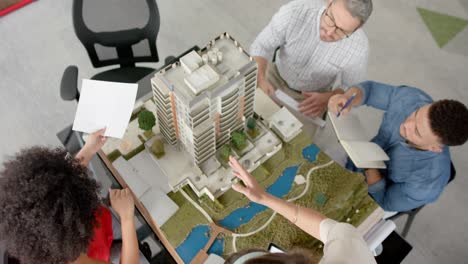 Overhead-view-of-team-of-diverse-engineers-discussing-over-a-3d-building-model-at-office