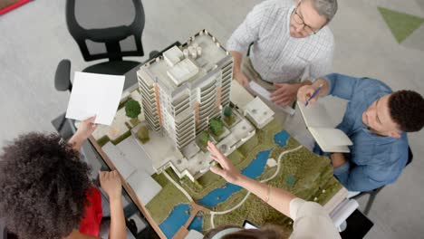 overhead view of team of diverse engineers discussing over a 3d building model at office