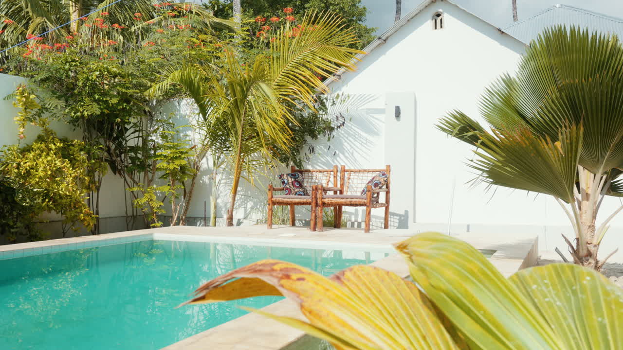 Two inviting chairs by a turquoise pool in a private spa, bathed in sunlight amidst tropical surroundings