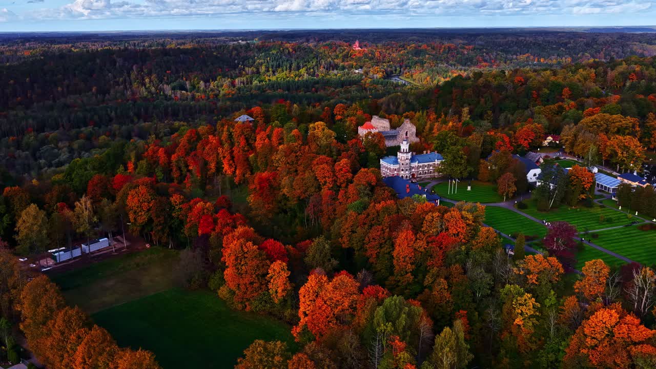 Aerial pullback of forest filled with orange foliage and countryside homes in quaint European landscape