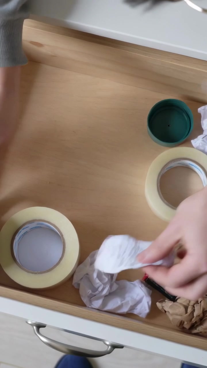 Vertical video: Reaching into wooden drawer, hands in grey top picking cutter, sorting masking tape
