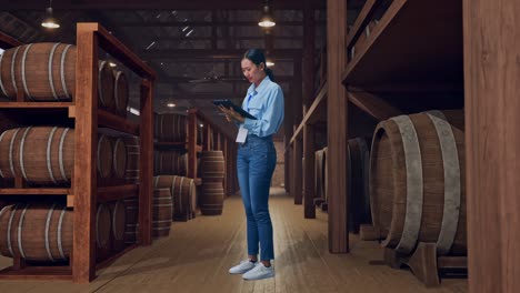 full body side view of an asian female professional worker standing with her tablet in cellar of winery, she is nodding her shead with dissapionted