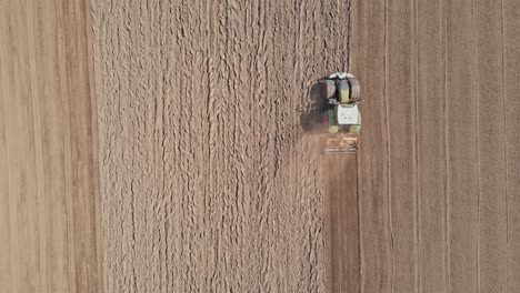 Top-down-aerial-of-tractor-plowing-empty-field-and-kicking-up-dirt-and-dust