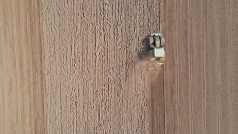 top down aerial of tractor plowing empty field and kicking up dirt and dust