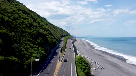 Carretera-Costera-Que-Se-Curva-A-Lo-Largo-De-Una-Exuberante-Ladera-Y-Playa,-Mar-Azul-En-Un-Día-Soleado,-Toma-Aérea