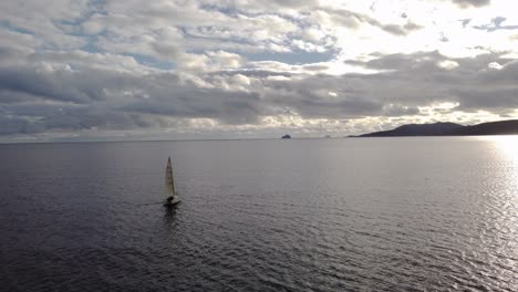 dramatic sky over the sea with a sailboat sailing towards land, aerial