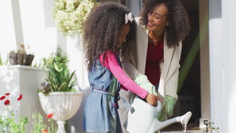 Glückliche-Afroamerikanische-Mutter-Mit-Tochter,-Die-Gemeinsam-Pflanzen-Gießt