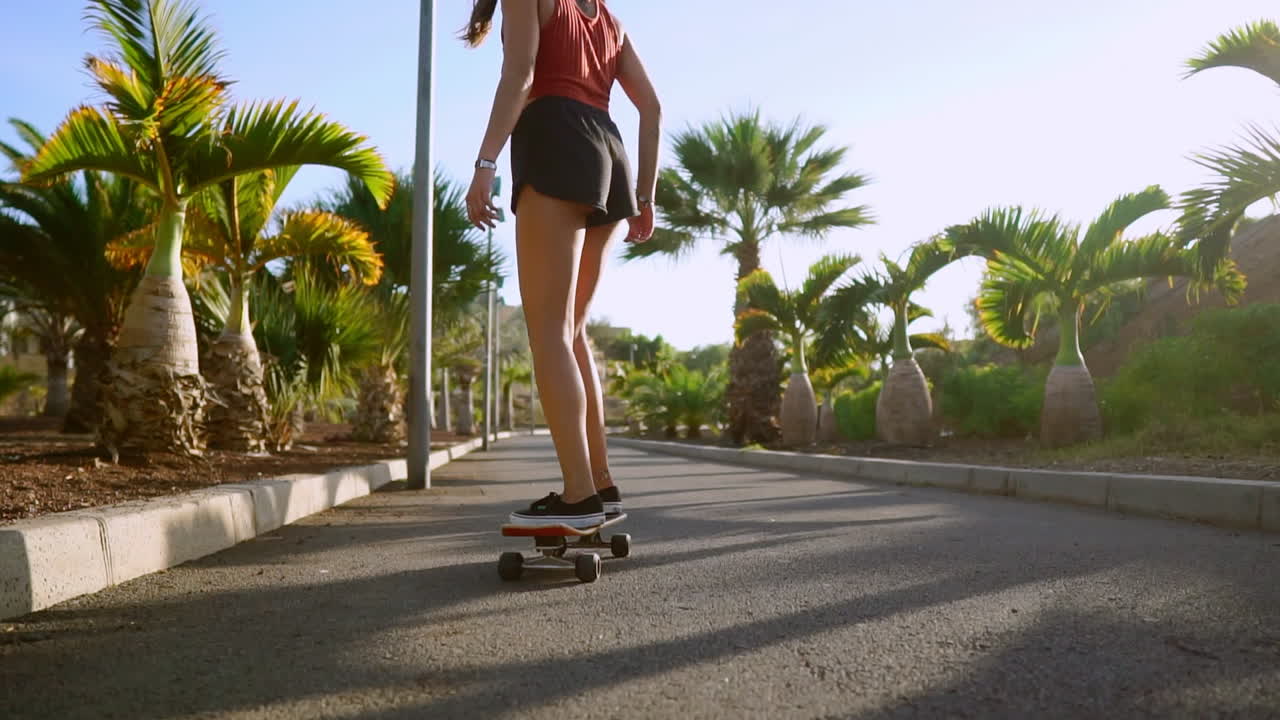 A woman, wearing a smile, rides her skateboard along the palm-bordered path in the park during sunset, the sandy surroundings amplifying her contentment. Happy people living well