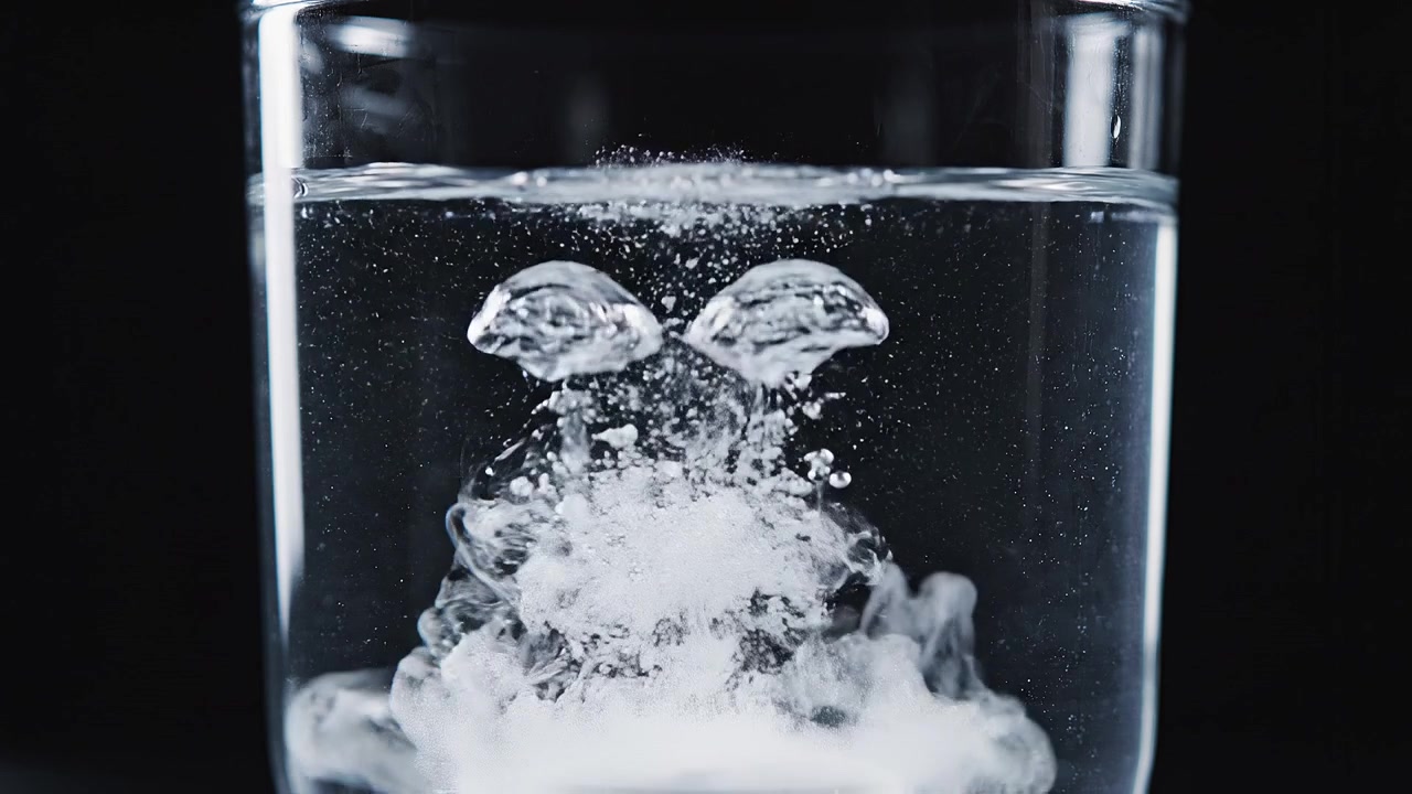 Compressa effervescente che cade in un bicchiere d'acqua limpida