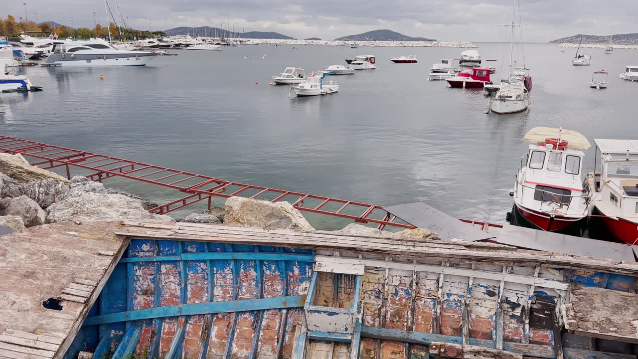 Scrap wooden row boat standing on the rocks on the sea shore in autumn in cloudy weather.