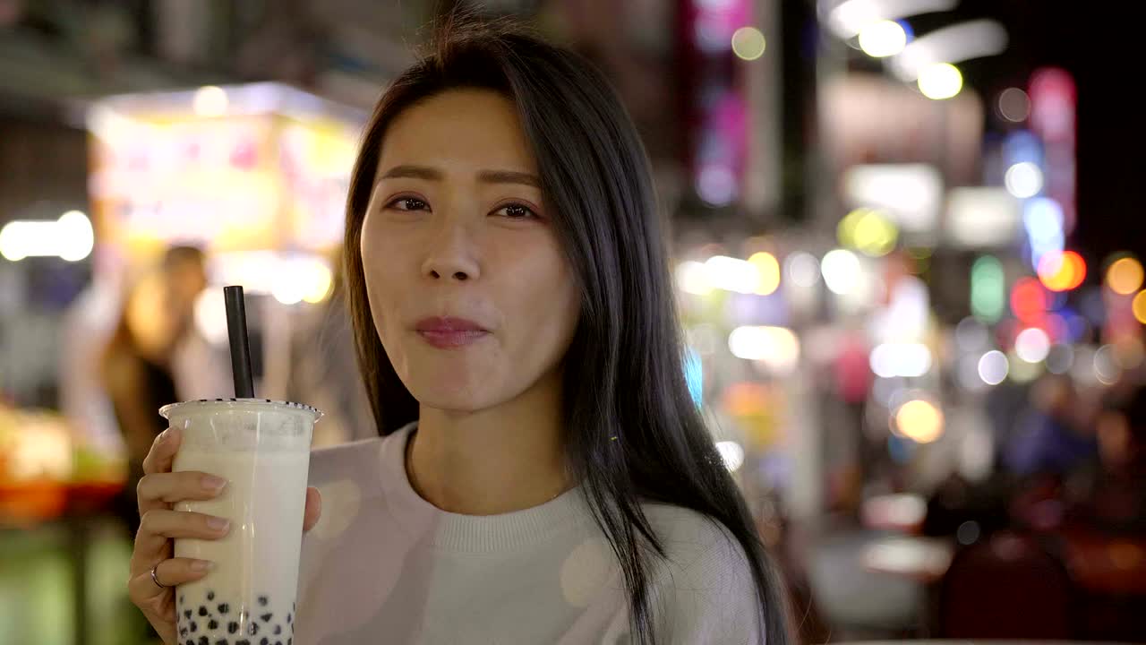 Wanita Asia menikmati teh susu boba dengan jajanan kaki lima di Pasar Malam