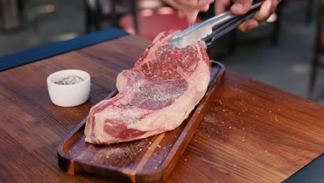 person seasoning steak with salt and pepper panning