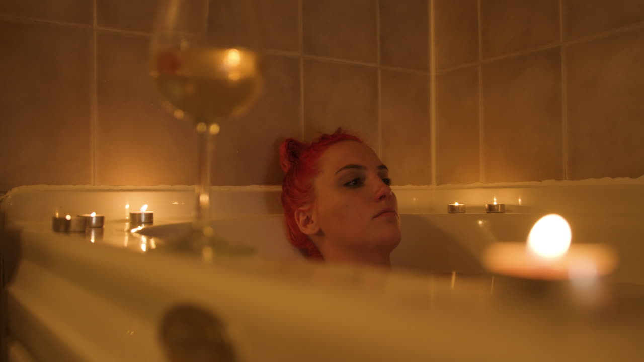 Sad young blonde woman relaxes in a warm bathtub with a glass of wine. Close up shot.