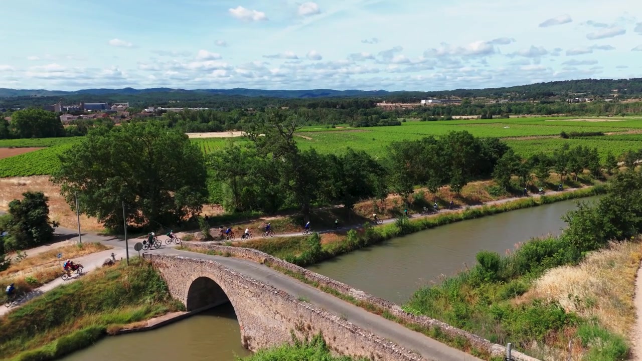 Vista aérea de ciclistas recorriendo el histórico Canal du Midi y cruzando un antiguo puente de piedra en el sur de Francia