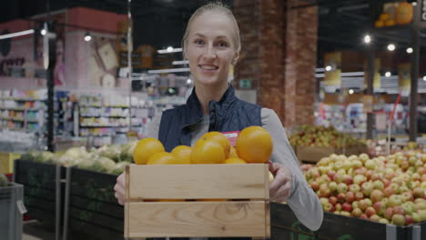woman holding a wooden crate of oranges in a grocery store