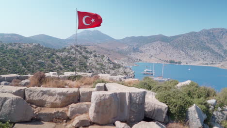 Turkish-flag-waves-in-slow-motion-on-hilltop-overlooking-boats-in-bay