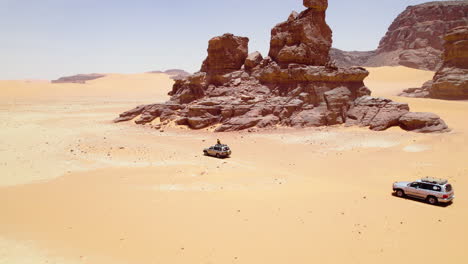 vehicles driving around the sand dunes of the sahara desert in algeria - aerial drone shot