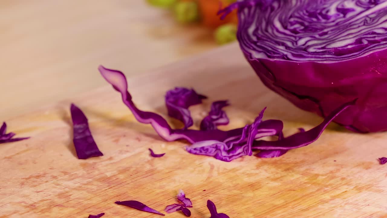 Hands skillfully chopping purple cabbage on a wooden board, showcasing detailed knife work and vibrant vegetable textures.