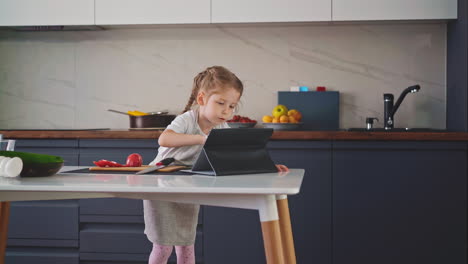 una niña se para en la cocina con un delantal en la mesa