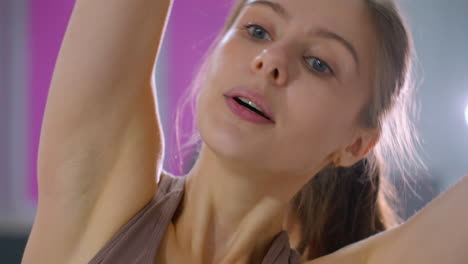 primer plano de una mujer realizando un estiramiento lateral durante una sesión de entrenamiento, luces brillantes del gimnasio brillan detrás de ella, iluminando su expresión enfocada mientras mantiene su forma y postura
