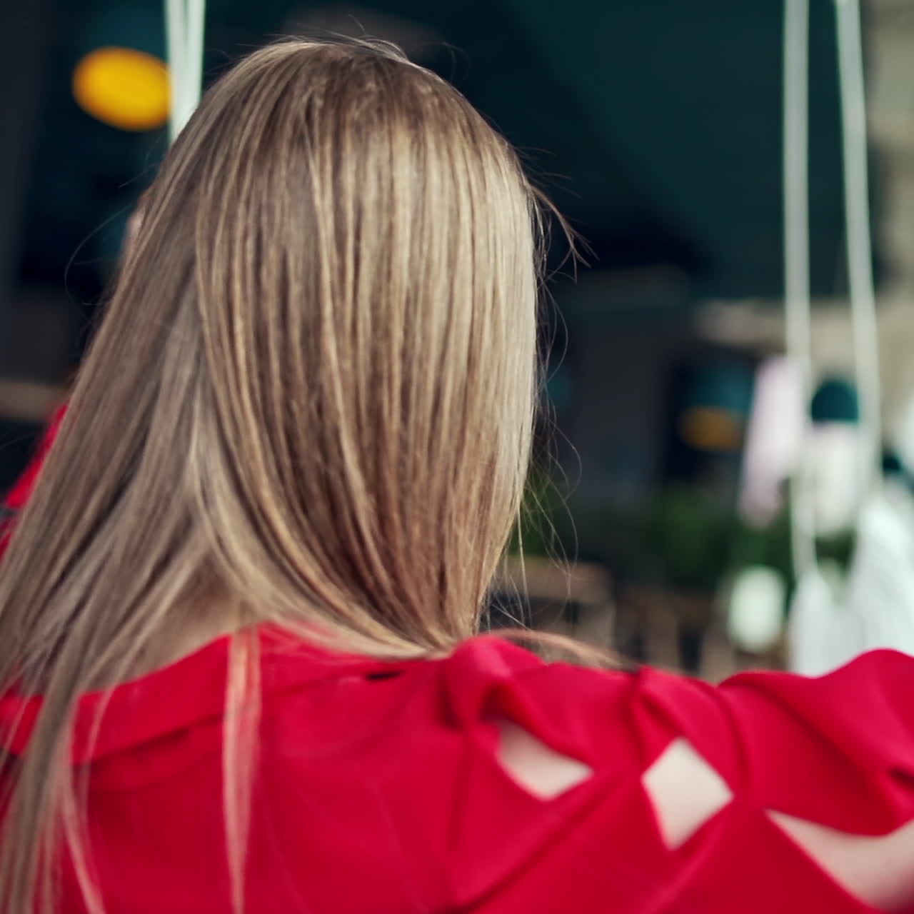Young happy woman relaxing at swing. Beautiful girl sitting on a swing and enjoying time alone. Close-up. Slow motion.