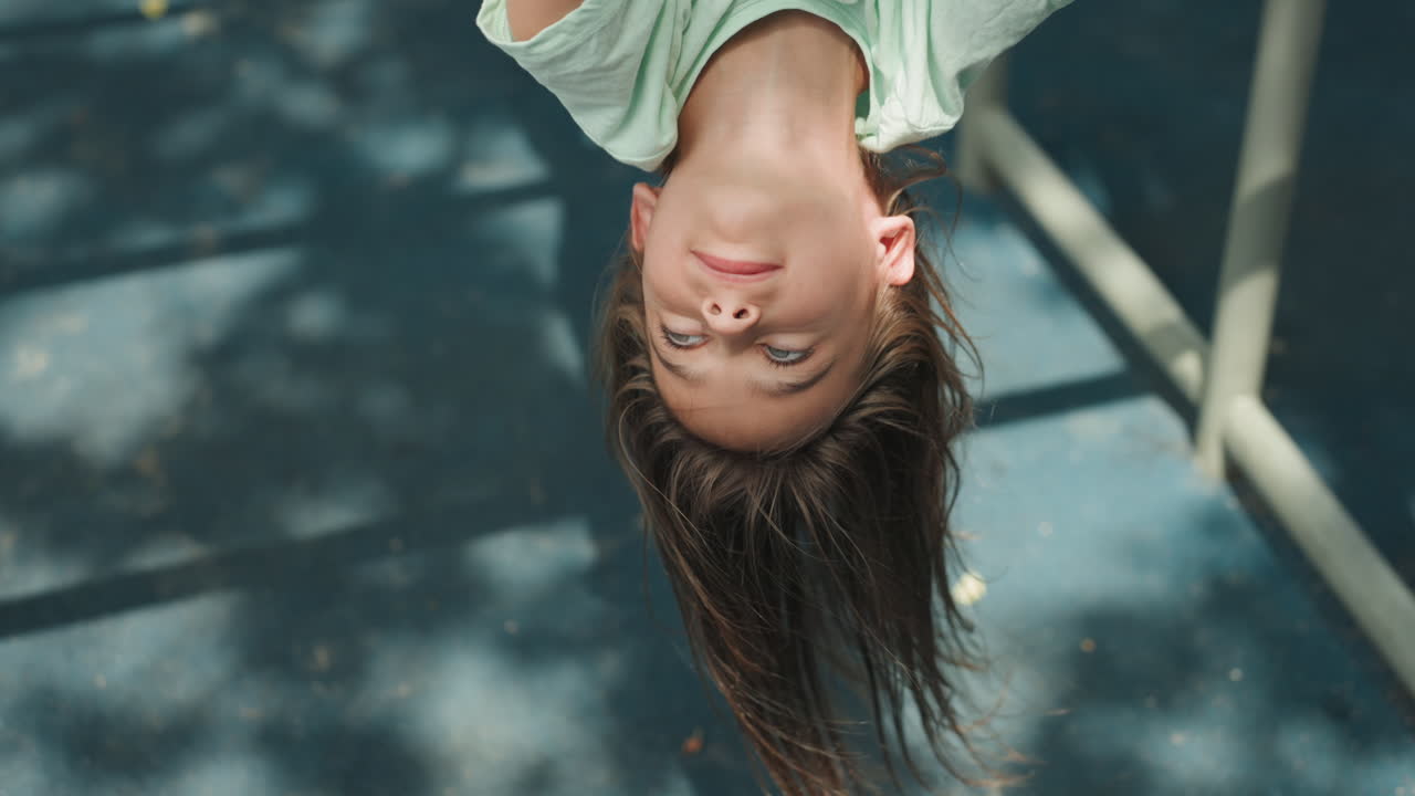 Daughter inverted closeup portrait under trees, braided hair hanging down and soft sunlight dappled across face, calm gaze and gentle expression, childhood wonder and quiet play, serene summer mood