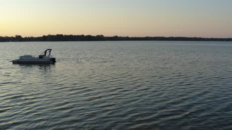 forward moving drone shot of a lake at sunrise from the dock, passing by a person with a camera