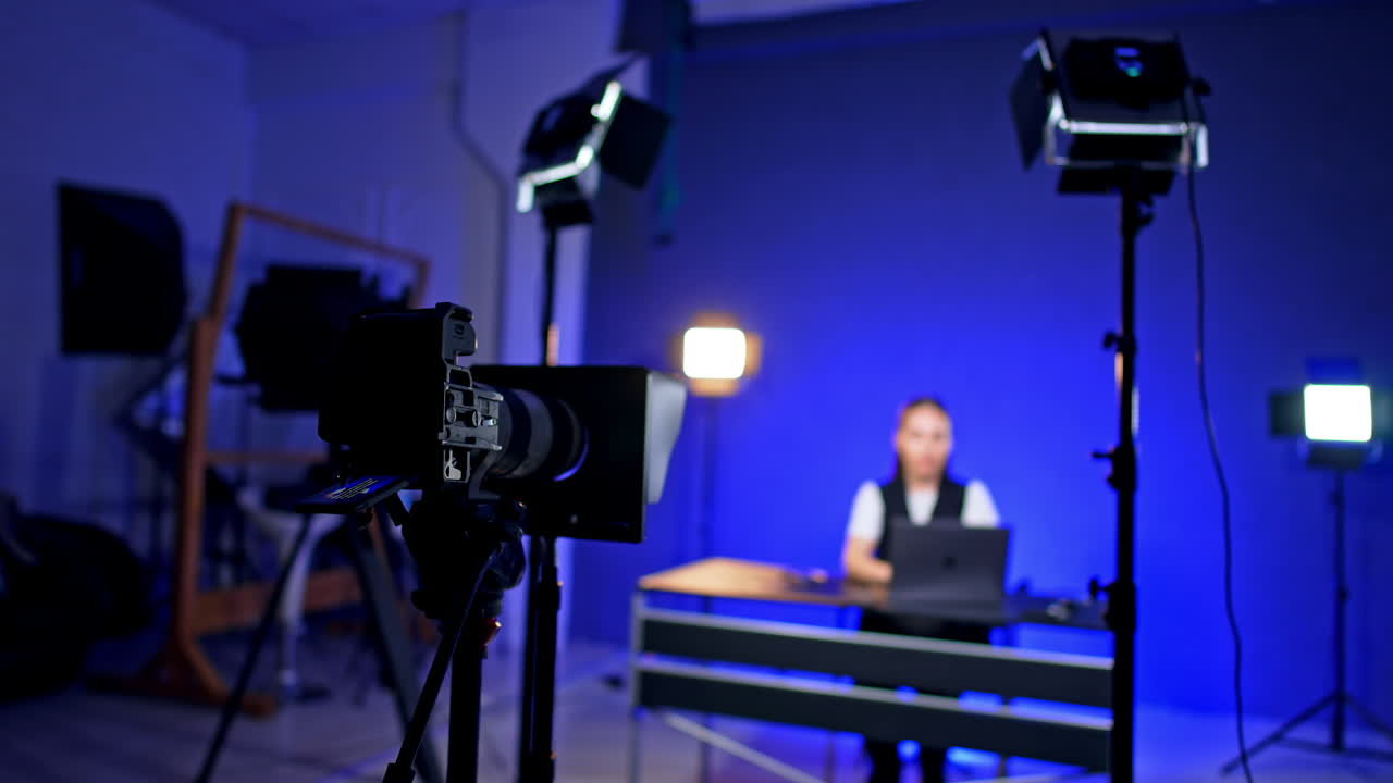 Hand of unrecognized cameraman touches a working camera on tripod. Female blogger recording a video blog at blurred backdrop.