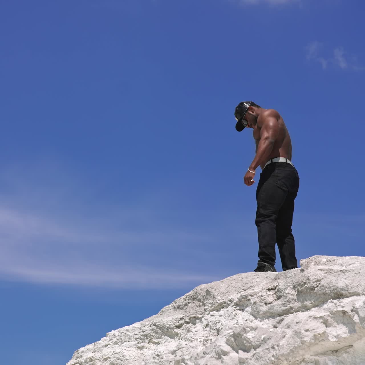 African american sportsman posing on blue sky background. Dark skinned athlete showing his strong arm muscles outdoors. View from below