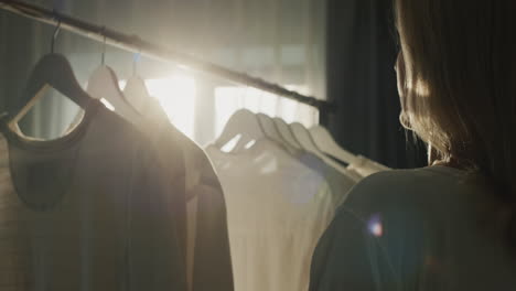 a woman hangs clothes on a rack, her silhouette beautifully illuminates the sun from the window