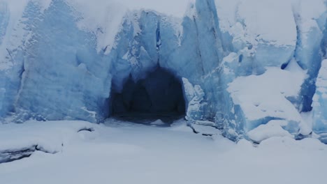 flying out of glacier cave in snowy landscape of alaska, backwards aerial shot