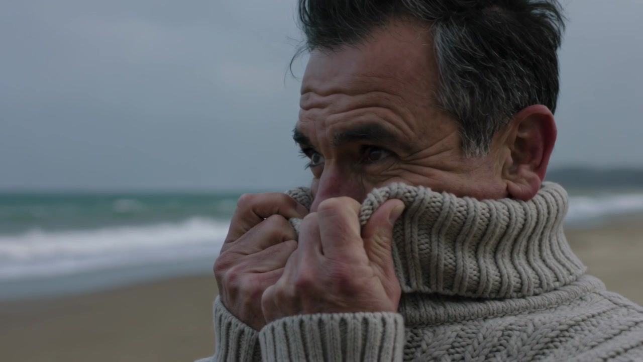 Feeling wind, middle-aged man pulling ribbed collar up at windy beach, blocking spray, copy space