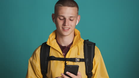 Young-blond-guy-with-backpack-using-smartphone