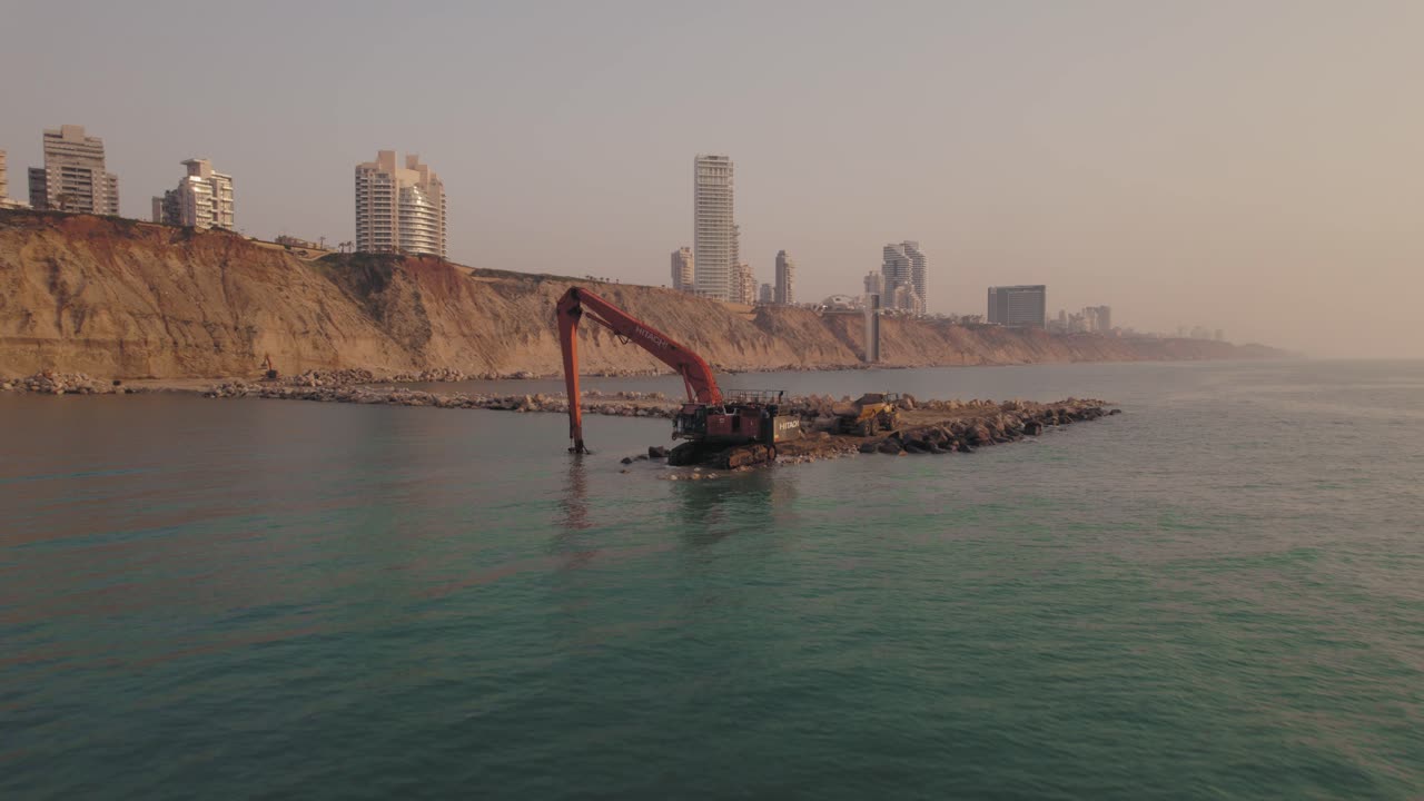 una sola máquina excavadora construye un rompeolas en el mar, tira hacia atrás al atardecer