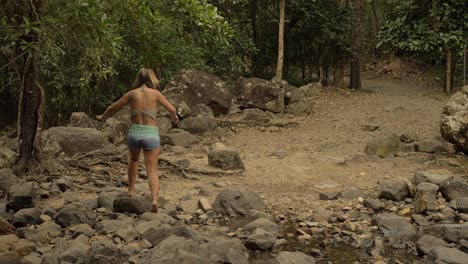 girl on denim shorts walking on rocks in cedar creek falls national park, queensland, australia