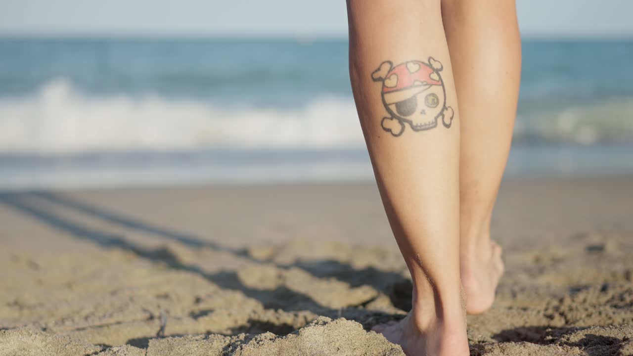 Persona che cammina a piedi nudi su una spiaggia sabbiosa con un tatuaggio di un teschio pirata