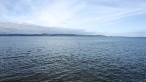 Calm-waves-on-a-beach-looking-across-the-water-to-an-island-|-Edinburgh,-Scotland-|-4k-at-30-fps