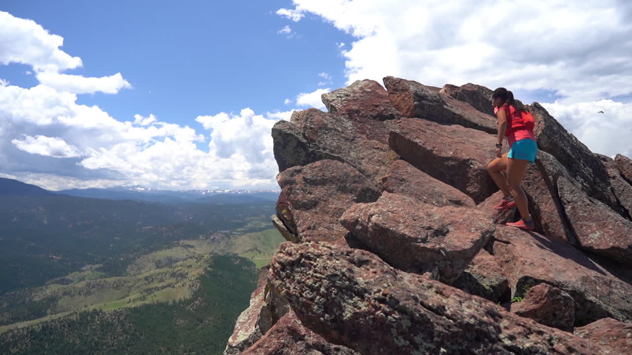 joven mujer asiática escalando en la cima de la roca sobre el abismo y el paisaje verde bajo un hermoso cielo en un día soleado de verano