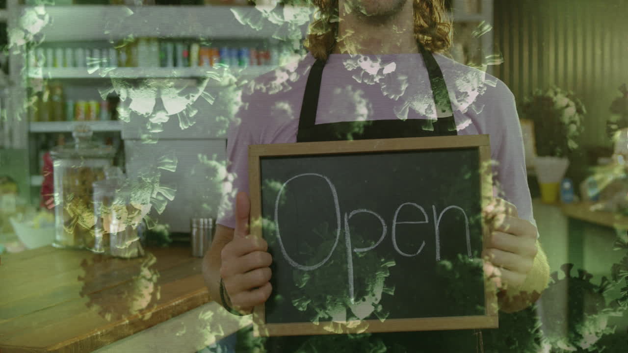 Animation of macro Covid-19 cells floating over happy Caucasian male chef holding Open sign