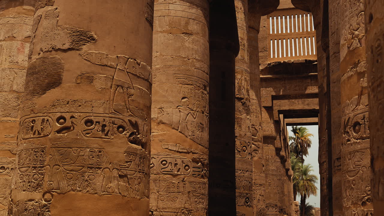 Stone pillars at Karnak Temple in Luxor, Egypt, lined with inscriptions and hieroglyphs. A sunny day highlights the ancient details of this iconic archaeological site