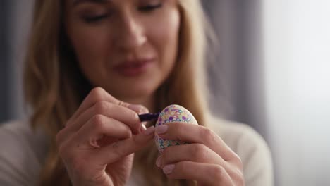 vista frontal de cerca de una mujer caucásica alegre decorando huevos de pascua en la cocina doméstica.