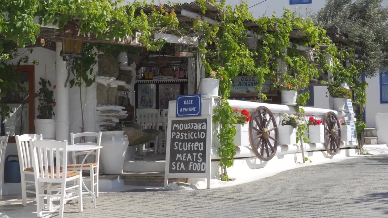 Quaint whitewashed Greek restaurant with an outdoor dining area and menu in the picturesque village of Ano Mera, Mykonos.