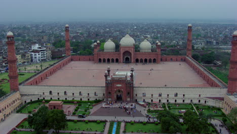 lahore, pakistan, drone view of world famous badshahi mosque, visitors are entering in the mosque, people are in the ground of the mosque, black kites flying, four minarets of the mosque