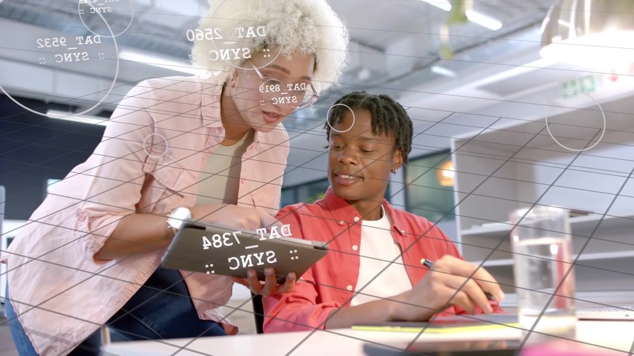 Standing woman approaching seated man at desk, showing tablet and mentoring with tech data overlay
