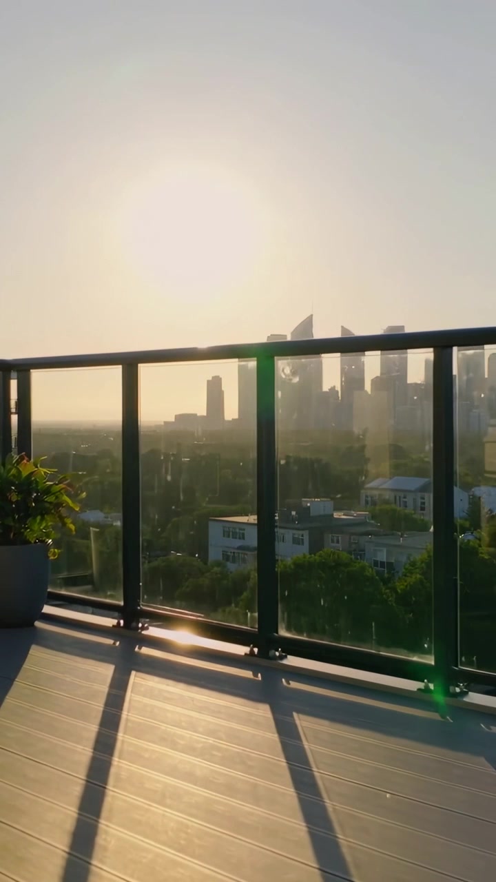 Video verticale: Sole che tramonta su una ringhiera di vetro di un balcone, proiettando ombre e un bagliore dell'obiettivo sullo skyline.
