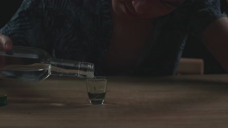 close up of drunk, depressed asian man pouring vodka in a shot glass before drinking and using a fist smashing the table in black background