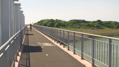 a young blonde girl cycling across a river on a bridge during the day