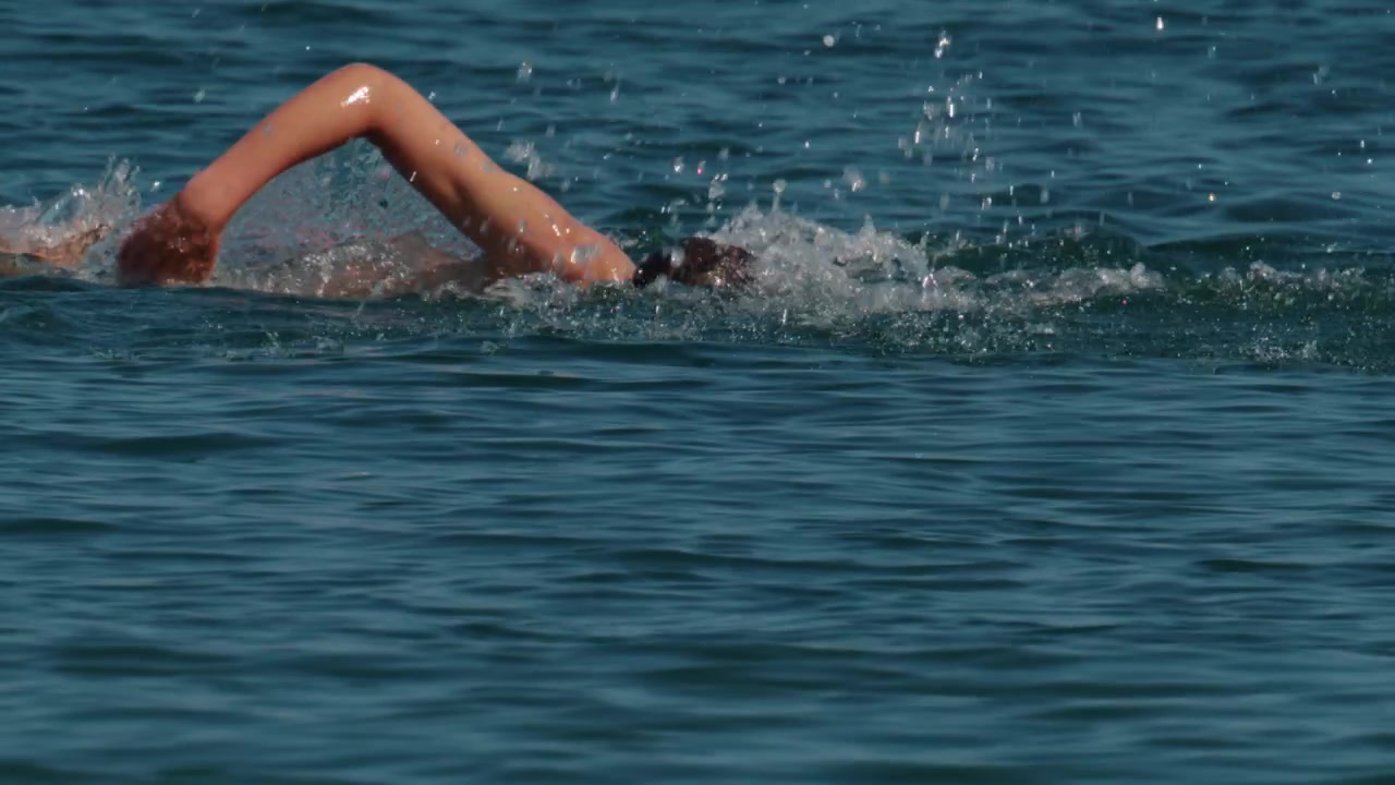 Sportler schwimmt Kraul, bewegt den Arm und erzeugt Spritzer im Meer während intensiven Trainings und Wettkampfs.
